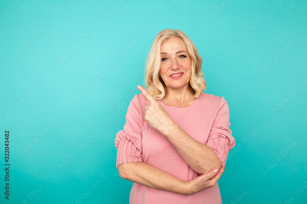 Portrait of cheerful adult woman pointing something in the blue background Portrait of cheerful adult woman pointing something in the blue background