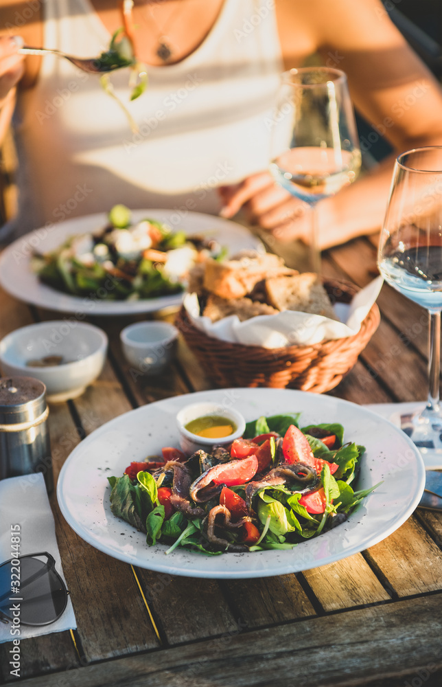 Young woman eating salad with seafood and drinking wine in summer open-air cafe in Italy with picturesque sea view background, selective focus. Travel, wanderlust, Italian lifestyle concept