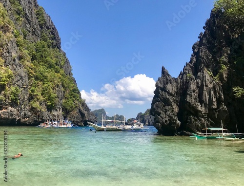 Bay with outrigger boats and woman floating in green and blue water, with islands in background, El Nido, Palawan, Philippines