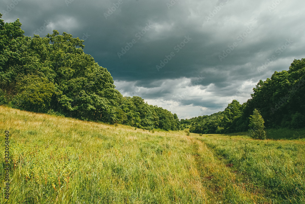 Obraz premium Picturesque and winding hills with fields, roads and dramatic pre-storm skies