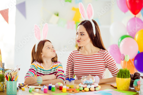 Close-up portrait of two nice attractive comic humorous playful cheerful girls small little pre-teen daughter wearing bunny ears holding pencil pout lips grimacing in white light interior room house