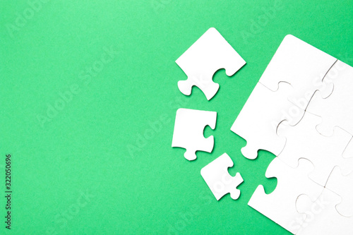 unfinished puzzle made of white cardboard on a green background, several parts are close, one piece is missing, copy space, search for some suitable part, team building concept