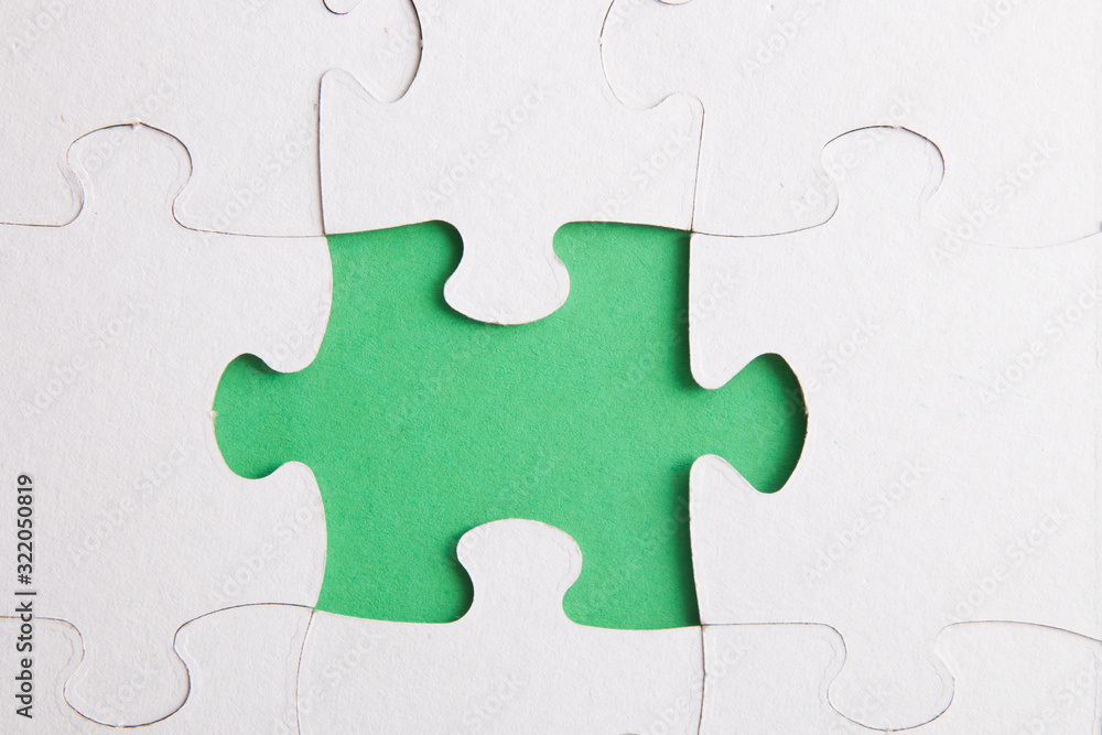 unfinished puzzle made of white cardboard on a green background and one unsuitable part from another puzzle, one piece is missing, copy space unfinished puzzle made of white cardboard on a green background and one unsuitable part from another puzzle, one piece is missing, copy space