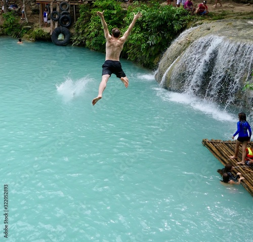 Man jumping from cliff into natural pool before waterfall , in air, cambugahay falls, Siquijor, Philippines