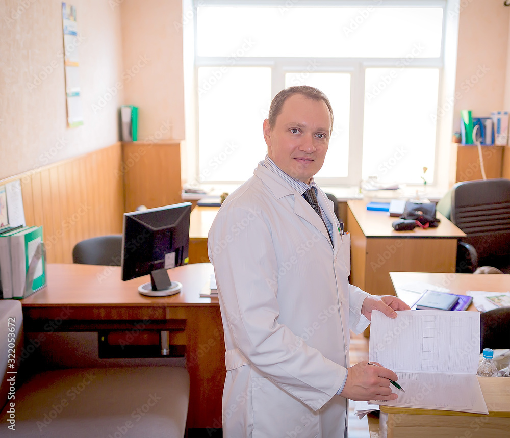 young attractive doctor in a white coat writes the patient’s story in the office of his clinic