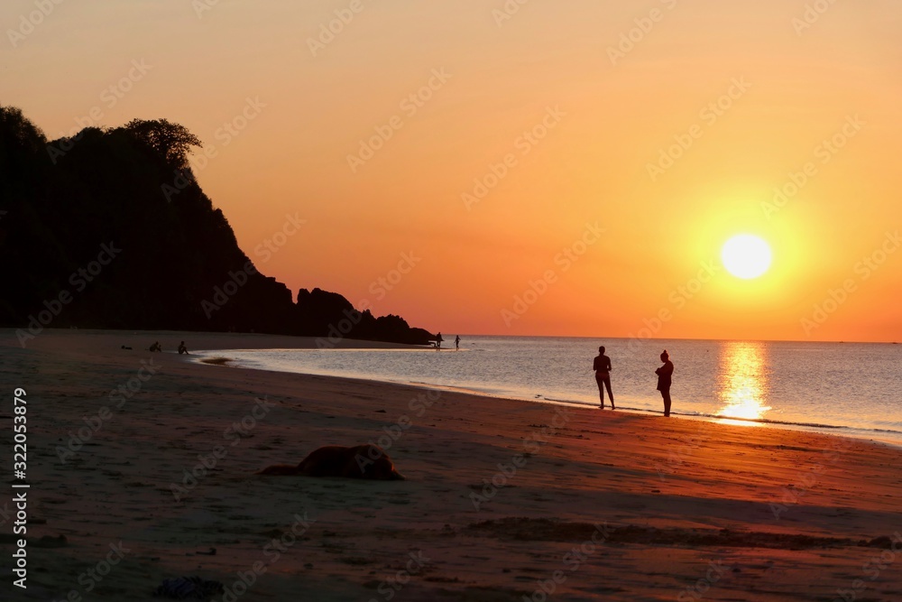 Sunset with orange sky at Nacpan beach with two girls and sleeping dog, El Nido, Palawan, Philippines Sunset with orange sky at Nacpan beach with two girls and sleeping dog, El Nido, Palawan, Philippines