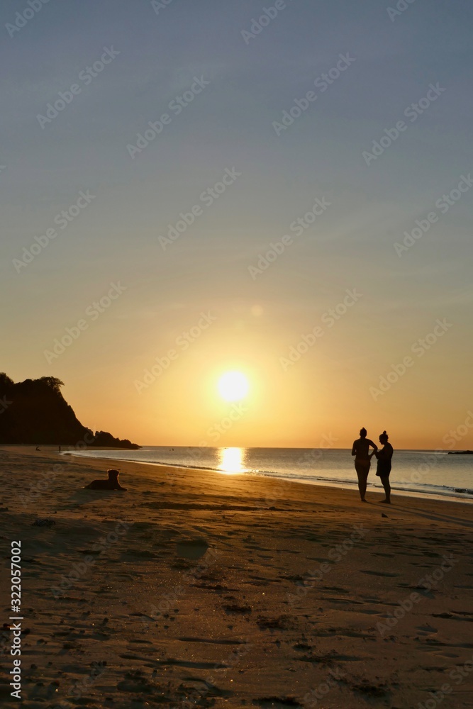 Sunset with orange sky at Nacpan beach with two girls and sitting dog, El Nido, Palawan, Philippines
