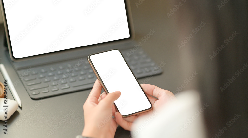 Close up image of the hand of a businesswoman is using a blank screen smartphone with a laptop. Close up image of the hand of a businesswoman is using a blank screen smartphone with a laptop.