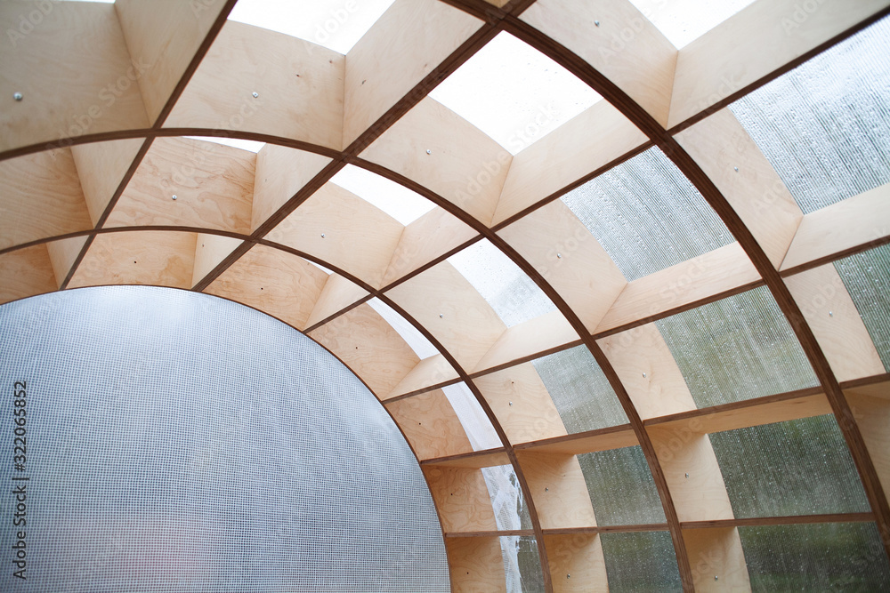 Obraz premium Abstract arched wooden frame with plastic walls to protect from wind and rain. Street temporary construction with geometrically regular shapes from wooden guides