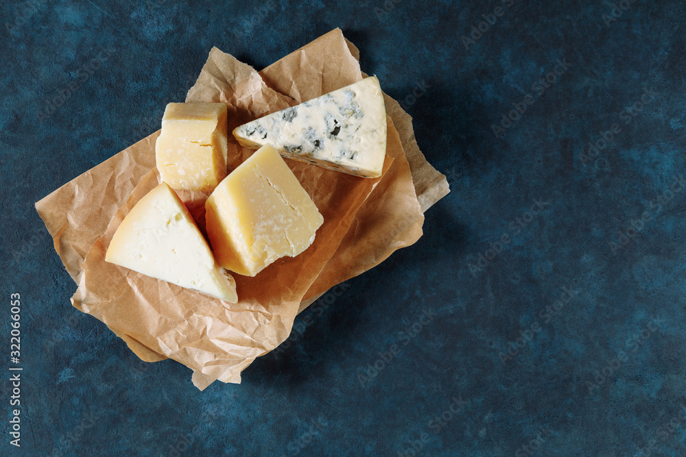 Different sorts of cheese on a parchment paper on dark blue textured background Different sorts of cheese on a parchment paper on dark blue textured background
