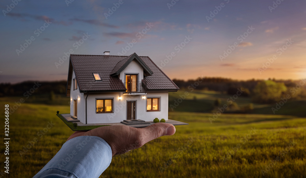 Obraz premium Concept of buying or building new home. Male hand showing, offering a new dream house at the empty field with copy space