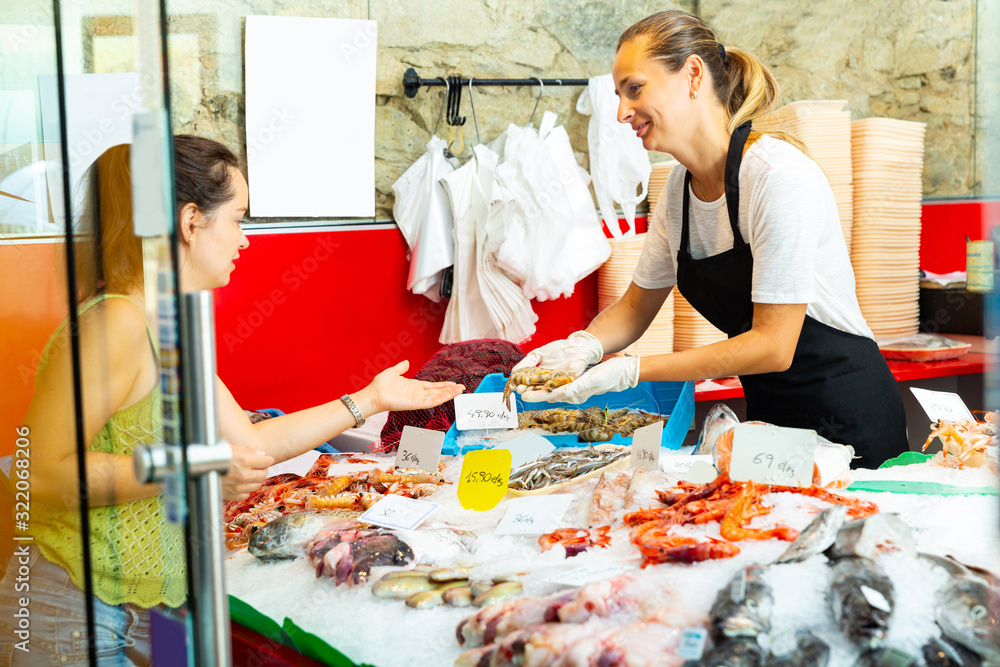 worker of fish shop offering fresh raw langoustines to customer