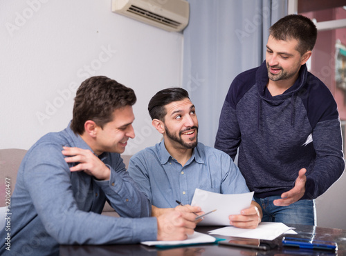 Three cheerful men reading documents at table