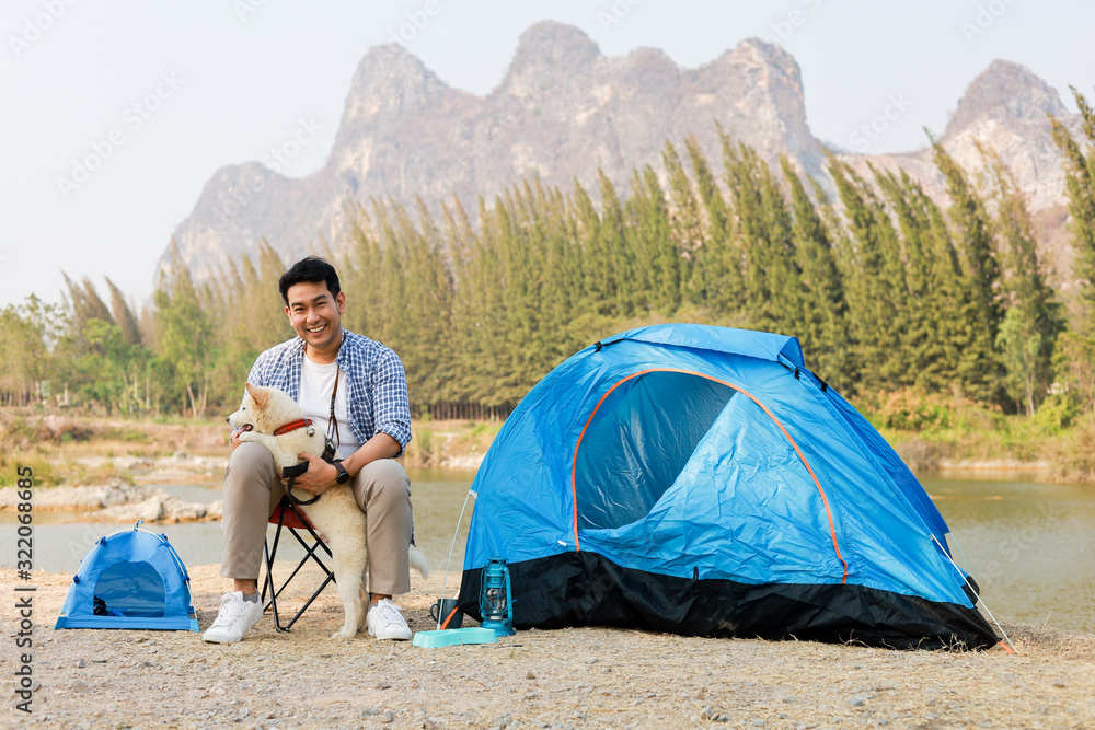 Asian young man in blue shirt with cute puppy dog camping on the lake hill mountain view happy and enjoy life Asian young man in blue shirt with cute puppy dog camping on the lake hill mountain view happy and enjoy life