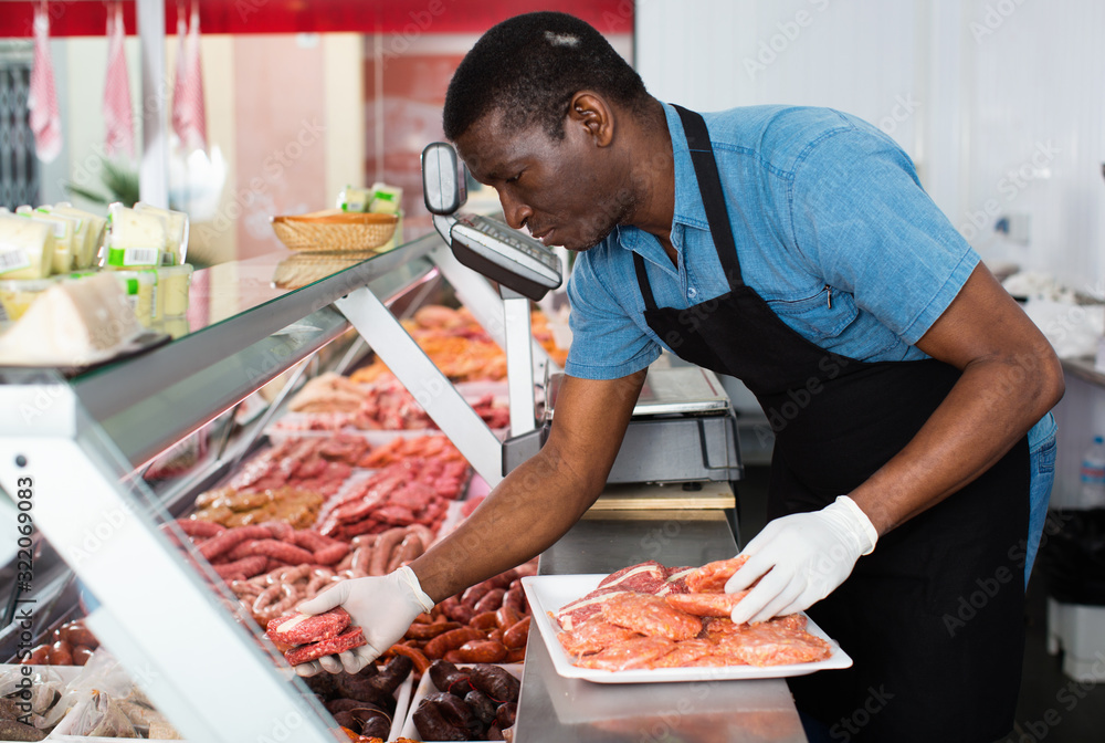 African American seller preparing fresh meat of lamb for sale in butcher store