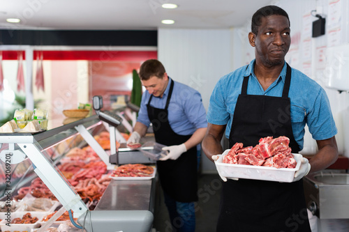 Successful owner of butcher store with his worker preparing fresh meat products for sale