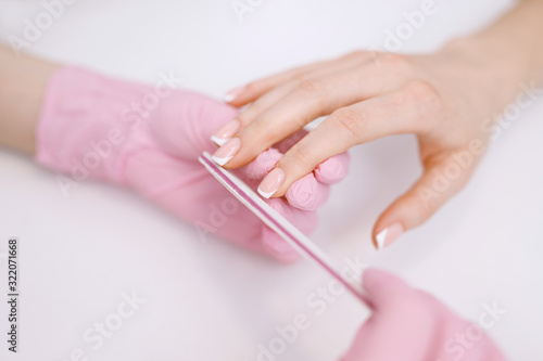 Closeup young well-groomed female hands. Manicurist doing professional manicure. Master files nails to client.