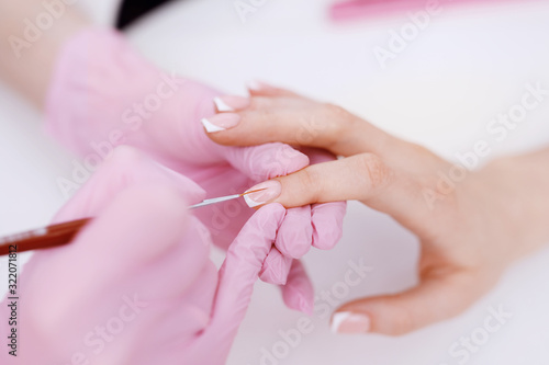 Closeup young well-groomed female hands. Manicurist doing professional manicure. Master applies nail polish to client.