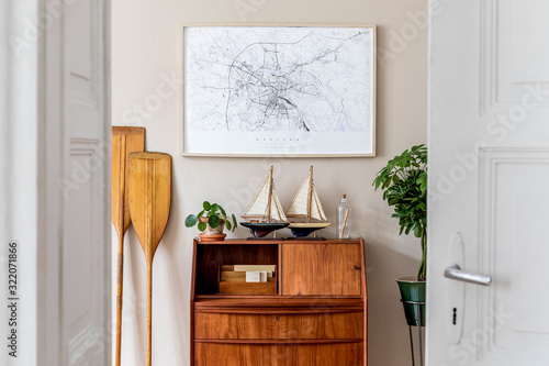 Stylish and vintage interior design of living room with wooden retro commode,  plants, ships, paddle, map and elegant personal accessories. Mock up poster frame on the wall. Template. Home decor.