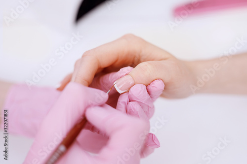 Closeup young well-groomed female hands. Manicurist doing professional manicure. Master applies nail polish to client.