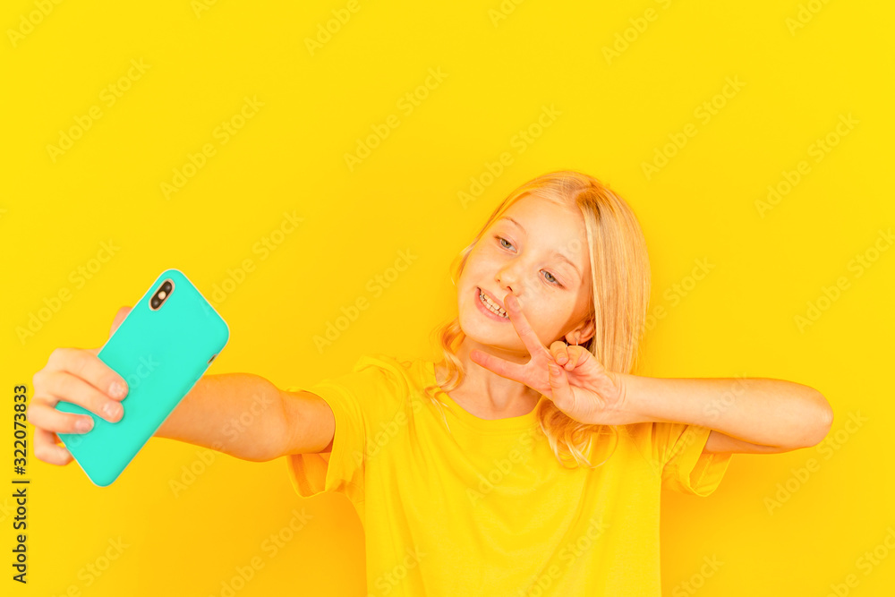 Smiling little girl kid showing blue screen of new popular mobile phone on light yellow background Smiling little girl kid showing blue screen of new popular mobile phone on light yellow background