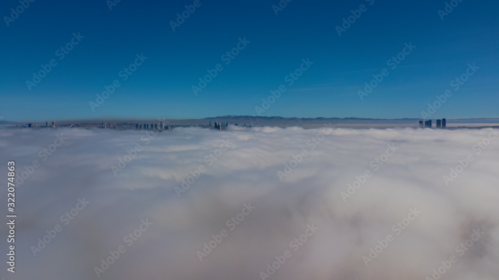 Landscape over the clouds in foggy weather. Hills of buildings in foggy weather. The drone and the top of the fog layer.