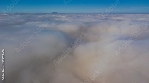 Landscape over the clouds in foggy weather. Hills of buildings in foggy weather. The drone and the top of the fog layer.