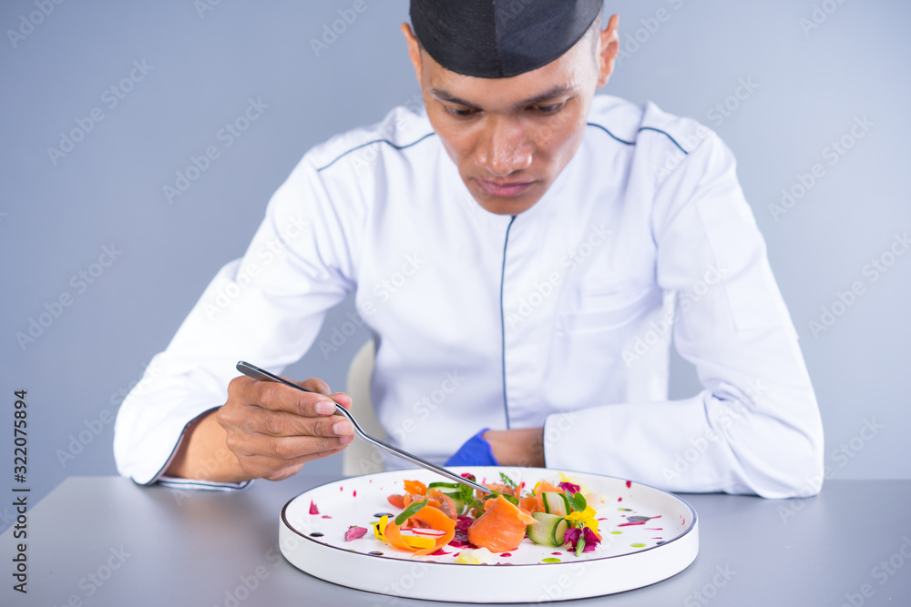 An Asian Executive Chef plating his dish carefully putting his finishing touch to the vibrant dish. An Asian Executive Chef plating his dish carefully putting his finishing touch to the vibrant dish.