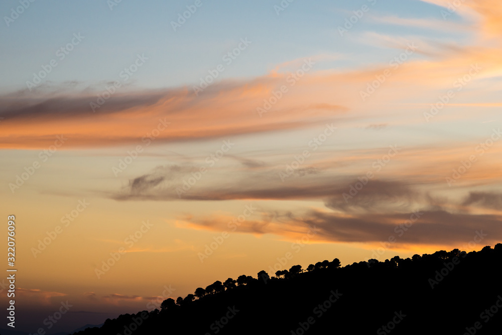 Sunset with clouds and silhouettes of trees in southern Spain.