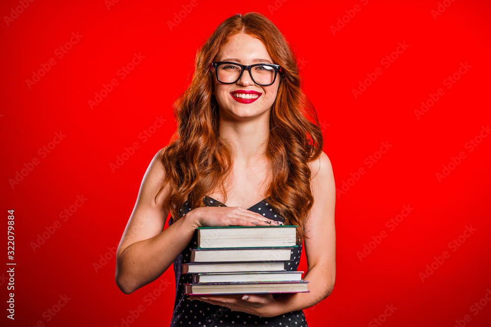 European student on red background in studio holds stack of university books from library. Woman smiles, she is happy to graduate. European student on red background in studio holds stack of university books from library. Woman smiles, she is happy to graduate.