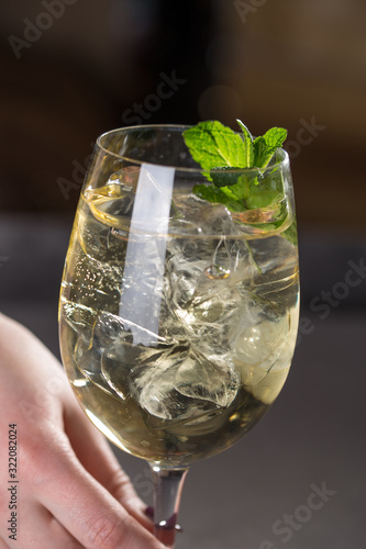 hand holding Hugo cocktail aperitif drink with Prosecco wine, lemon, mint and melissa syrup on dark background photo