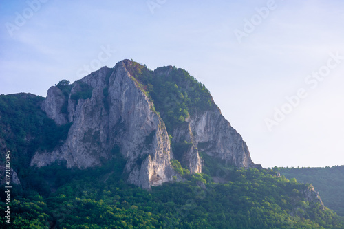 rock formation on the field at sunrise. beautiful rural landscape in mountains. wonderful scenery in spring. clouds on the blue sky. forest on the hills