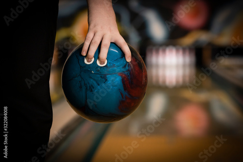 ten pin bowling ball being held in hand by bowler close up, with bowling lane and ten pins blurred in the background, copy space