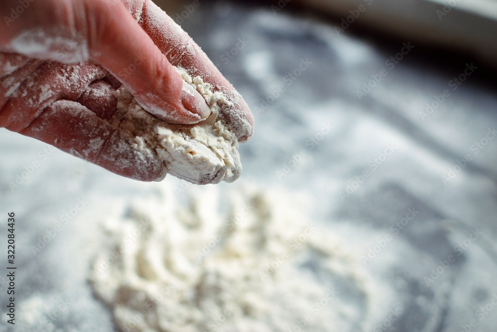Fototapeta premium Flour in the hands of a woman. A woman pours flour on a black board. Ingredients, baking process.