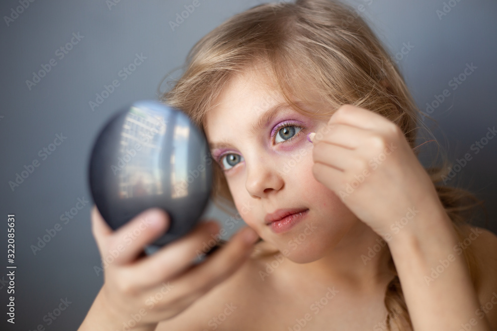 charming child, little beauty, cute girl of 7-8 years old with beautiful blond curls, make-up, mom’s makeup at the table, gray background charming child, little beauty, cute girl of 7-8 years old with beautiful blond curls, make-up, mom’s makeup at the table, gray background