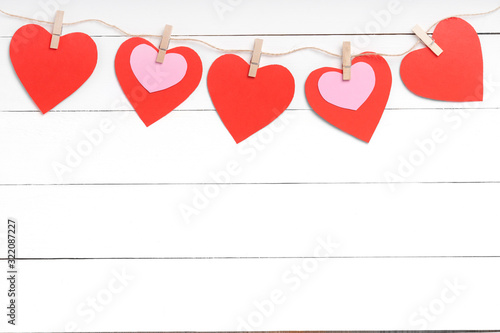 Clothespins with red hearts hanging on rope behind white wooden surface.
