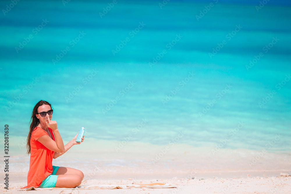 Beautiful young woman holding a suncream lying on tropical beach Beautiful young woman holding a suncream lying on tropical beach