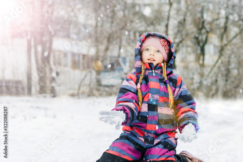 Little beautiful girl sits in a park in the snow. Surprised by the snowfall.