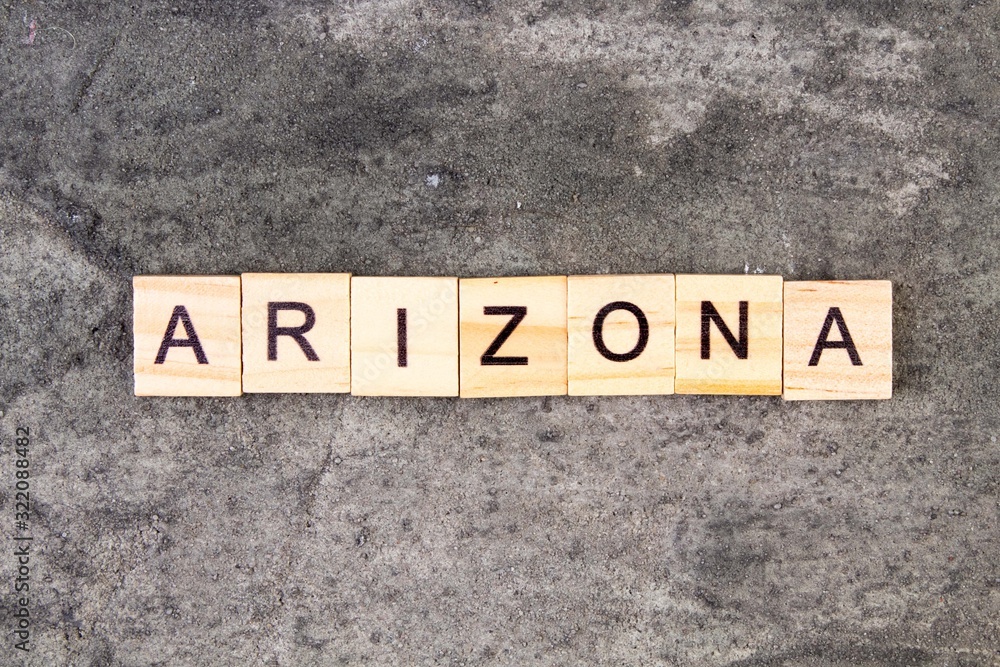 Arizona word written on wood block, on gray concrete background. Top view. Arizona word written on wood block, on gray concrete background. Top view.