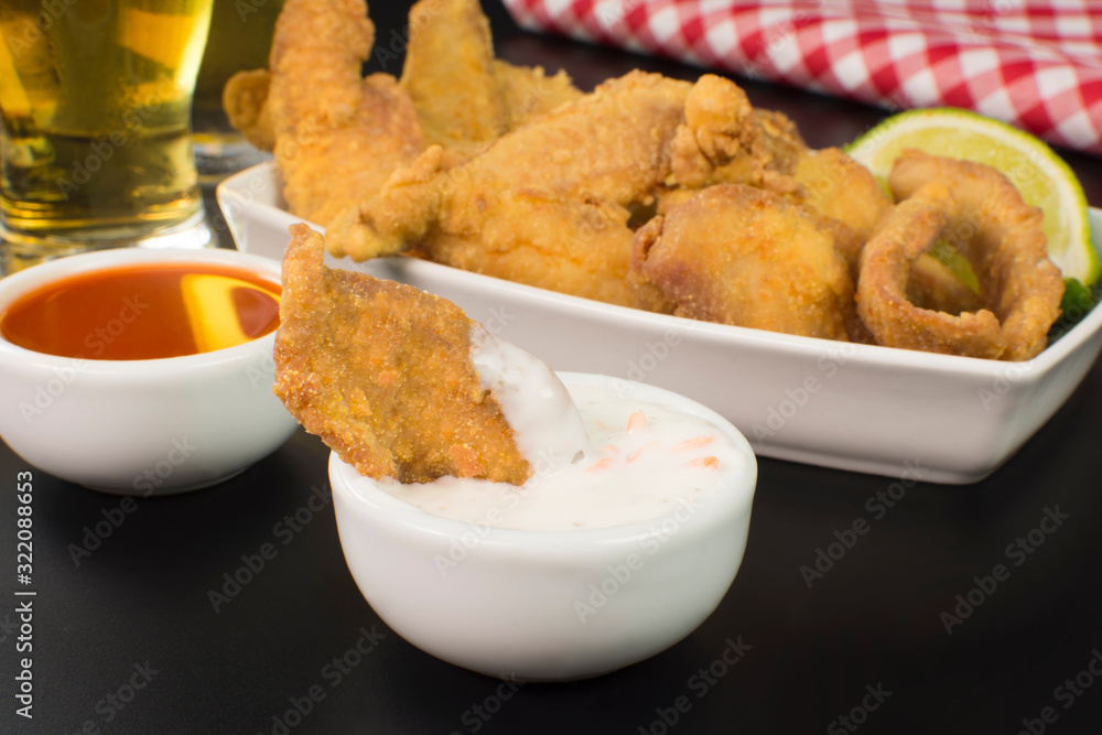One fried tilapia strip in a bowl with tartar sauce close with a