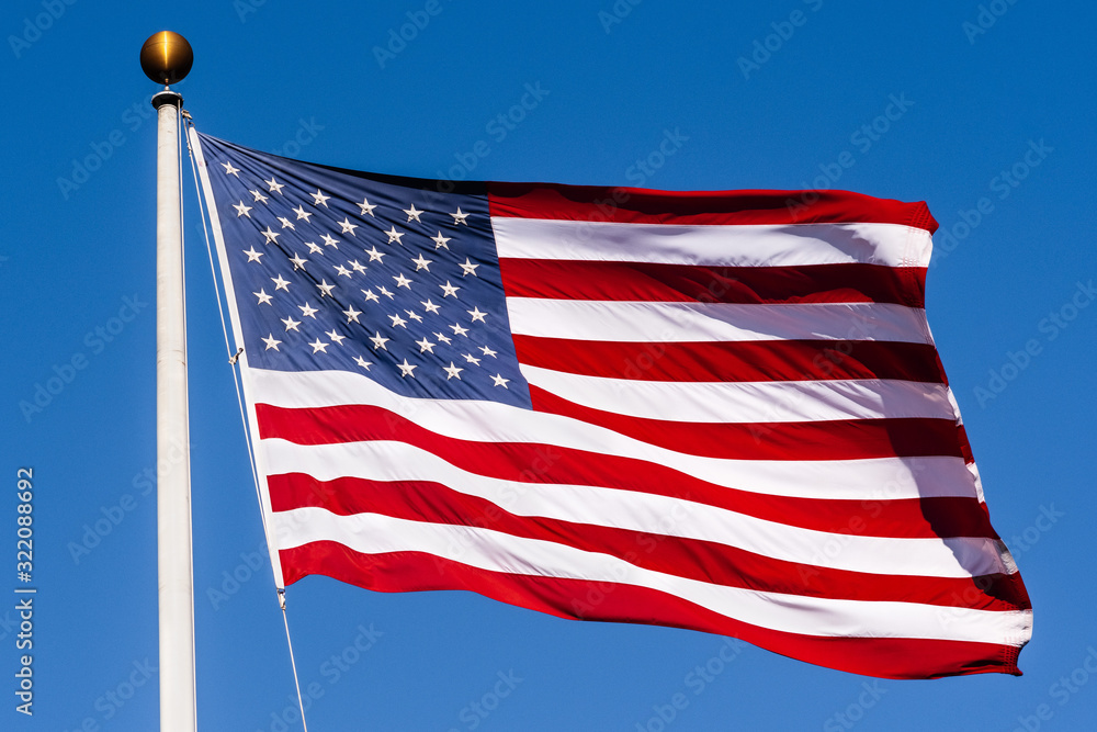 Fototapeta premium Beautifully waving star and striped American flag on a blue sky background; Close Up for Memorial Day or 4th of July
