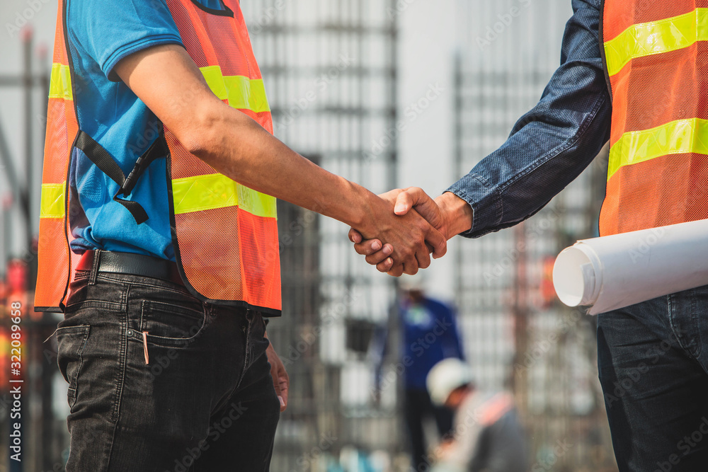 Hanshake seals an agreement at construction site. Architect and worker handshaking on construction site. building, teamwork, partnership, gesture and people concept. Hanshake seals an agreement at construction site. Architect and worker handshaking on construction site. building, teamwork, partnership, gesture and people concept.