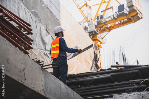 Engineer in hardhat and orange jacket posing on building site. civil engineer or architect with hardhat on construction site checking schedule on plan.