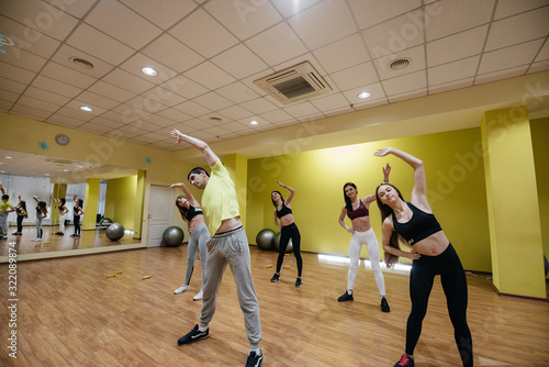 Fototapeta Naklejka Na Ścianę i Meble -  A group of young athletic girls perform exercises in the gym under the guidance of a coach. Healthy lifestyle