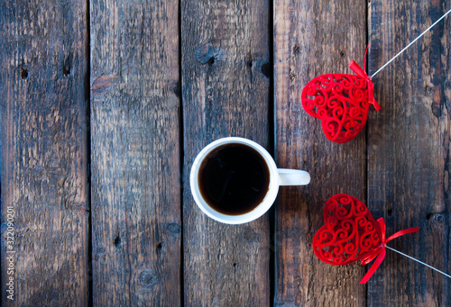 Red heart on a stick and a white cup with tea or coffee. On a wooden table. View from above