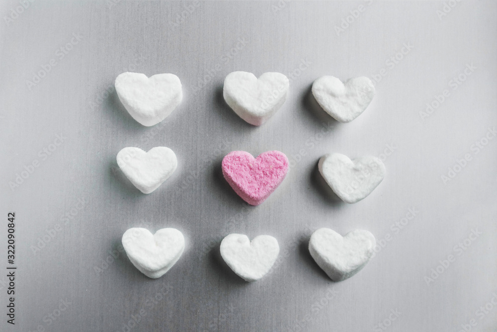 pink marshmallow heart lies among white sugar marshmallows square shaped on gray aluminum background