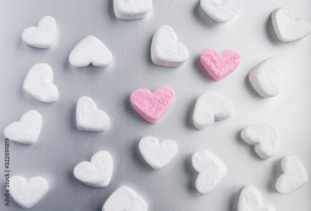 two pink marshmallow hearts lies among white sugar marshmallows in the shape of hearts evenly laid out on a gray aluminum background two pink marshmallow hearts lies among white sugar marshmallows in the shape of hearts evenly laid out on a gray aluminum background