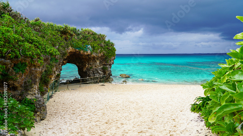 Travel to famous Paradise beach of Sunayama on Miyako Island in Japan. Seascape against blue stormy sky before rain, bright birch water, snow-white sand and a stone cliff overgrown with greenery 