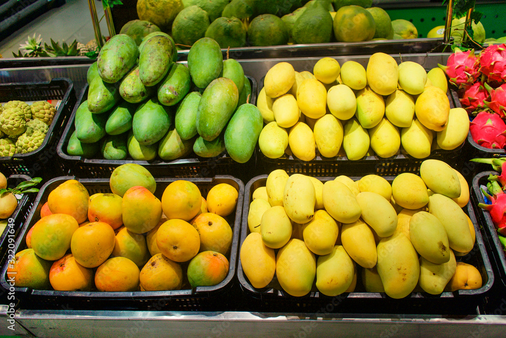 Exotic tropical fruits in the asian market. Different tipes of fresh ripe sweet mangoes. Yellow, orange and green mango. Healthy vegan raw food in the shop.