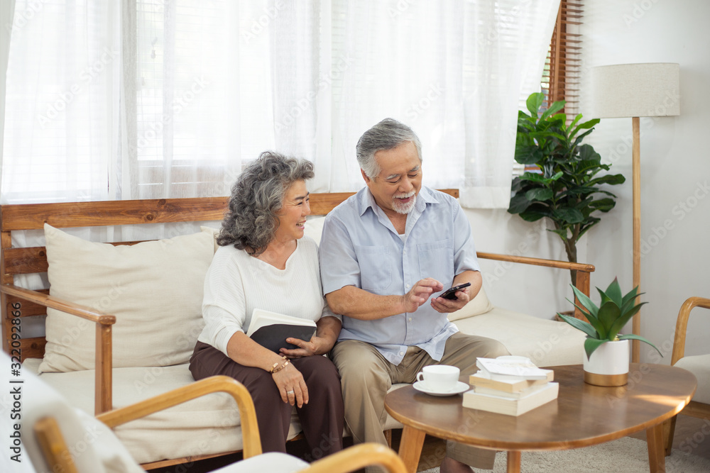 Happy Asian senior couple using smartphone together on couch in living room, older man texting message or chatting with family, elderly woman watching interested on gadget , Aging society concept Happy Asian senior couple using smartphone together on couch in living room, older man texting message or chatting with family, elderly woman watching interested on gadget , Aging society concept